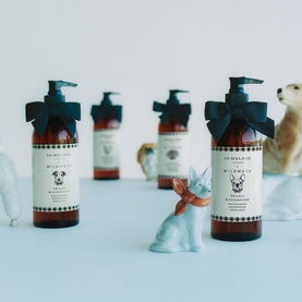 Jo Malone Wild Malva shampoo bottles with black ribbon bows, displayed alongside decorative animal figurines on a light blue surface