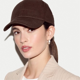 Model with Jigsaw brown corduroy baseball cap, worn with a neutral blazer and small hoop earrings