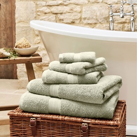 Christys Thyme bath towelling set of six folded towels stacked on wicker chest, freestanding bath in background