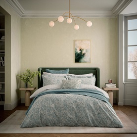 Teal and cream floral print duvet set styled on a green upholstered bed in a neutral bedroom with gold pendant light