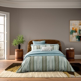 Teal and gold striped bedding set styled on a bed with brown velvet headboard, paired with patterned cushions in a warm-toned bedroom