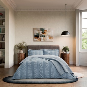 Blue seersucker duvet cover set styled on a double bed in a neutral bedroom, with matching pillowcases and textured stripe detail