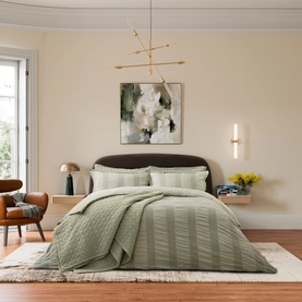 Sage green quilted bedding set styled on a double bed in a warm neutral bedroom with wooden flooring and abstract wall art