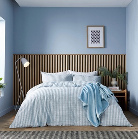 Light blue gingham check duvet set styled on a double bed with matching pillowcases and a blue throw, wooden slatted headboard backdrop