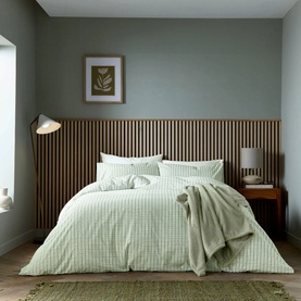 Sage green gingham check duvet set styled on a double bed with matching pillowcases, in a neutral wood-panelled bedroom setting.