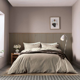 Neutral beige duvet set styled on a double bed with dark brown throw, wooden slat headboard, bedside table and wall light in a minimal bedroom.