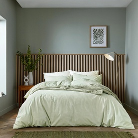 Sage green duvet cover and pillowcase set on a styled double bed, with wooden headboard panelling and neutral bedroom backdrop.