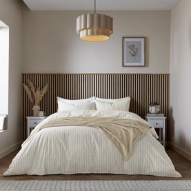 Cream striped duvet set styled on a double bed with matching pillowcases, in a neutral bedroom with wooden slat headboard panel