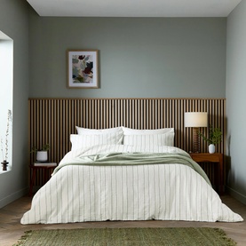 White and sage green stripe bedding set styled on a double bed with wooden slatted headboard, side tables and lamp in a calm bedroom setting.