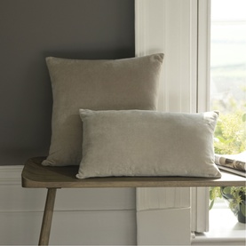 Christys brown velvet cushion covers in two sizes, styled on a wooden bench by a window in a neutral room setting.