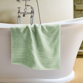 Christys green bath towel draped over the edge of a freestanding white bathtub in a bright bathroom setting