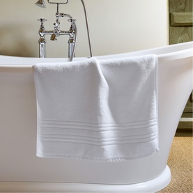 Christys white bath towel draped over a freestanding bathtub, featuring decorative border detailing, shown in a classic bathroom setting