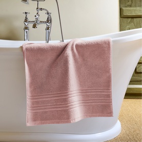 Dusty pink cotton bath towel draped over a freestanding white bathtub, with ribbed border detailing visible