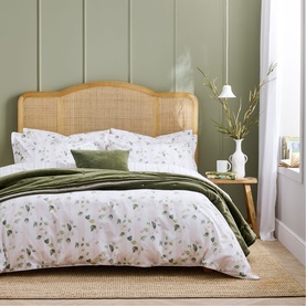Christys green floral duvet set styled on a rattan-headboard bed with olive velvet throw and matching pillows