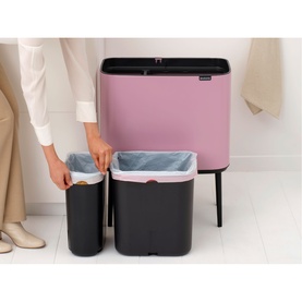 Brabantia Bo Touch Bin in Lilac Pink with open lid, styled next to a dark rectangular bin, hands placing liner inside