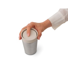 Brabantia soft beige cup with fitted lid, hand pressing down to secure the top, compact cylindrical design