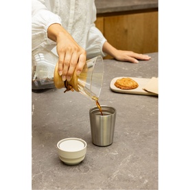 Brabantia soft beige cup on marble surface, with coffee being poured into a stainless steel travel cup alongside a ceramic lid