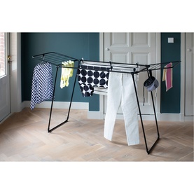 Brabantia Matt Black clothes drying rack with laundry items draped over rails, styled in a modern home setting with wooden flooring.
