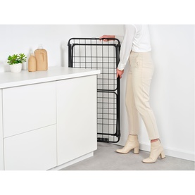 Model with Brabantia Matt Black wire rack being unfolded in a kitchen setting, styled with cream cabinetry and countertop