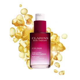Clarins L'Elixir Hair Oil in pink-to-red gradient bottle, surrounded by golden oil droplets on white background