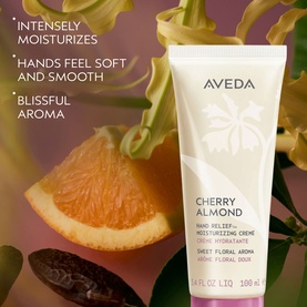 Aveda Cherry Almond Hand Relief Moisturizing Cr&egrave;me tube surrounded by orange slices, dates, and floral botanicals