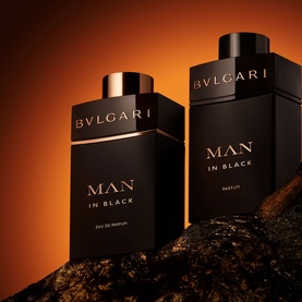 Bulgari Man In Black Eau de Parfum Gift Set, two black and rose gold bottles displayed on dark stones against a warm amber background.