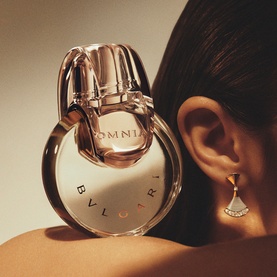 Bulgari Omnia Crystalline Eau de Toilette & Hand Cream Gift Set, circular gold-toned bottle with ring base shown close-up near model's ear
