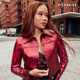 Model with Coach Cherry Parfum & Travel Spray Gift Set 50ML, wearing a red metallic leather jacket, holding the dark fragrance bottle