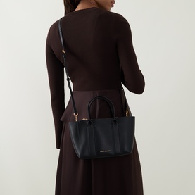 Model carrying Marc Jacobs The Small Work Tote Bag in black pebbled leather with gold-tone hardware and crossbody strap, styled with dark burgundy