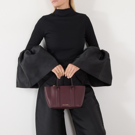 Model carrying Marc Jacobs The Small Work Tote Bag in Dark Port pebbled leather with dual top handles, styled with black wide-sleeve top and trousers