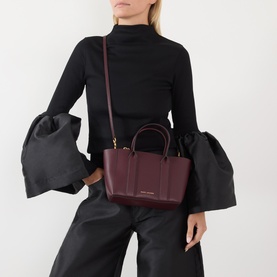 Model carrying Marc Jacobs The Small Work Tote Bag in Dark Port pebbled leather, gold-tone hardware, with crossbody strap, styled with black