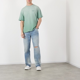 Model wearing Represent Washed Aloe cotton T-shirt, styled with light wash distressed jeans and white trainers.