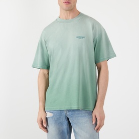Model wearing Represent T-Shirt in Washed Aloe, relaxed fit with small chest logo, styled with light blue jeans.