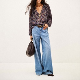 Model wearing Bash blue wide-leg jeans with a floral blouse and brown leather belt, carrying a dark brown hobo bag.