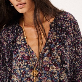 Model wearing Bash blue floral print blouse with V-neckline, styled with a gold chain pendant necklace