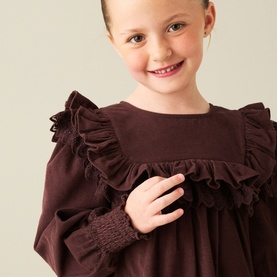 Model wearing Angel & Rocket Chocolate cotton dress with ruffle yoke detail and smocked cuffs, close-up lifestyle shot