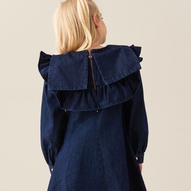 Model wearing Angel & Rocket Denim Blue cotton dress, shown from back, with large ruffle collar detail and long sleeves