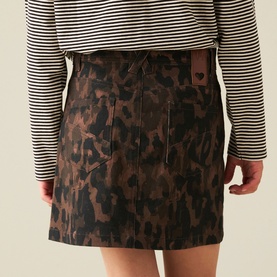 Model wearing a brown and black leopard print mini skirt with heart detail tab, styled with a striped monochrome top.