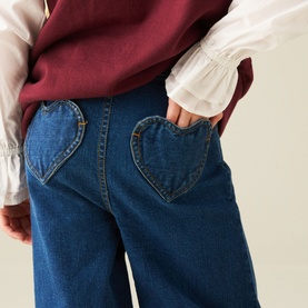 Model wearing Angel & Rocket Denim Blue wide-leg jeans with heart-shaped back pockets, styled with a white frill-sleeve top and burgundy vest.