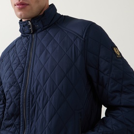 Model wearing Belstaff quilted casual jacket in Dark Ink navy, with buckle collar detail and embroidered logo badge on sleeve.
