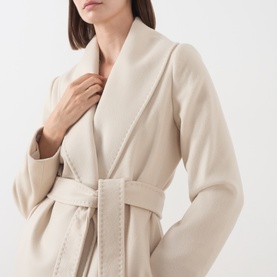 Model wearing Max Mara Studio ecru virgin wool coat with shawl collar, belted waist, and contrast topstitching detail.