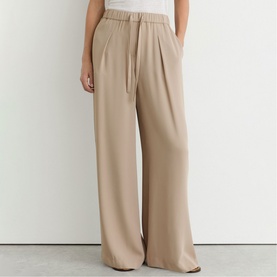 Model wearing Reiss beige wide-leg trousers with elasticated waistband and pleat detail, styled with a white top