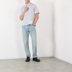 Model wearing Thom Browne med grey striped short-sleeve cotton shirt with red cuff stripe, styled with light wash jeans and black loafers.