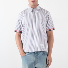Model wearing Thom Browne medium grey striped cotton short-sleeve shirt with red, white and blue ribbed cuffs, styled with light wash jeans
