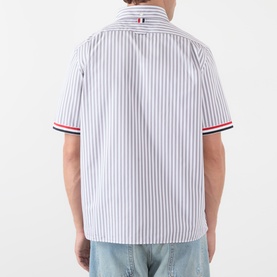 Model wearing Thom Browne medium grey striped cotton short-sleeve shirt, back view, with red and navy stripe cuff trim and blue jeans.