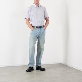 Model wearing Thom Browne med grey striped short-sleeve cotton shirt with red-tipped cuffs, styled with light wash jeans and black loafers.