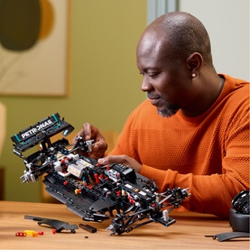 Man assembling Lego Technic Mercedes-AMG F1 car set in black, with loose pieces on wooden table