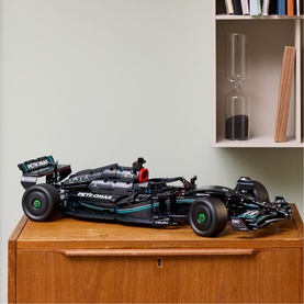 Lego Technic black Mercedes-AMG F1 car model displayed on a wooden sideboard, with hourglass and vase on shelf behind