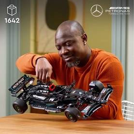 Lego Technic Mercedes-AMG F1 black 1642-piece model displayed with man in orange jumper assembling it on a table