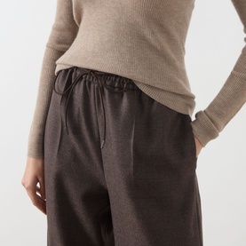 Model wearing Max Mara Main mud wool trousers with elasticated waist and drawstring, styled with a beige ribbed knit top.